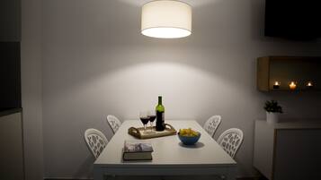 Un comedor con una mesa dispuesta para dos, que incluye una botella de vino, copas, un tazón de papas fritas y un libro.