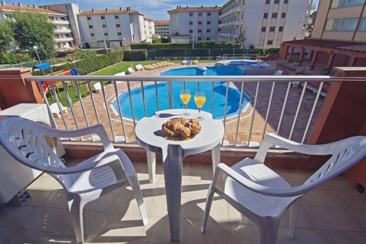Un balcón con piscina, sillas de plástico blanco y una mesa con comida y bebidas.
