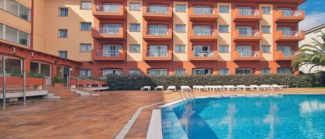 A hotel with a swimming pool, multiple balconies, and a tiled patio area.