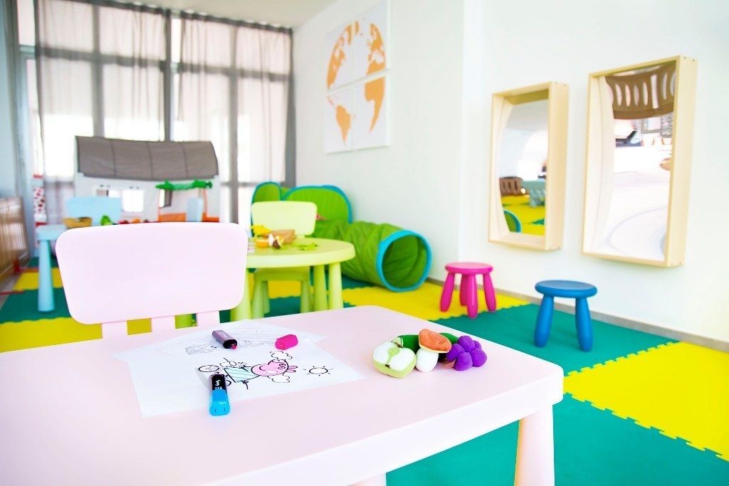 A children's playroom with a pink table, colorful toys, and a green play mat.