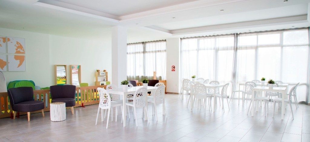 A spacious room with a large dining table surrounded by white chairs, a sofa, and a small round table with chairs.