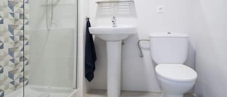 Un baño con cabina de ducha de vidrio, lavamanos pedestal y retrete.