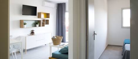 Een moderne, goed verlichte kamer met een wit bureau, een aan de muur bevestigde televisie en een raam dat natuurlijk licht binnenlaat.