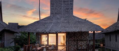 A resort with thatched-roof cottages, a central building with large windows, and a lush garden.
