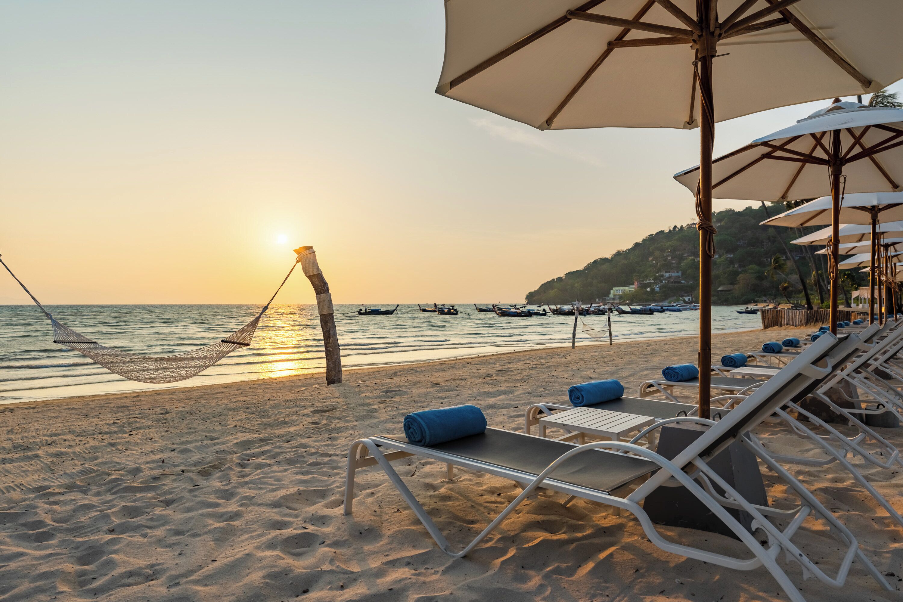 A beach with a hammock, lounge chairs, and umbrellas.