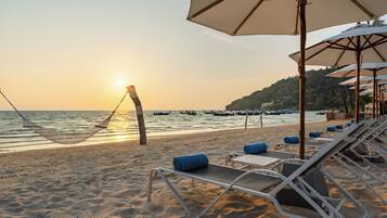 A beach with a hammock, lounge chairs, and umbrellas.