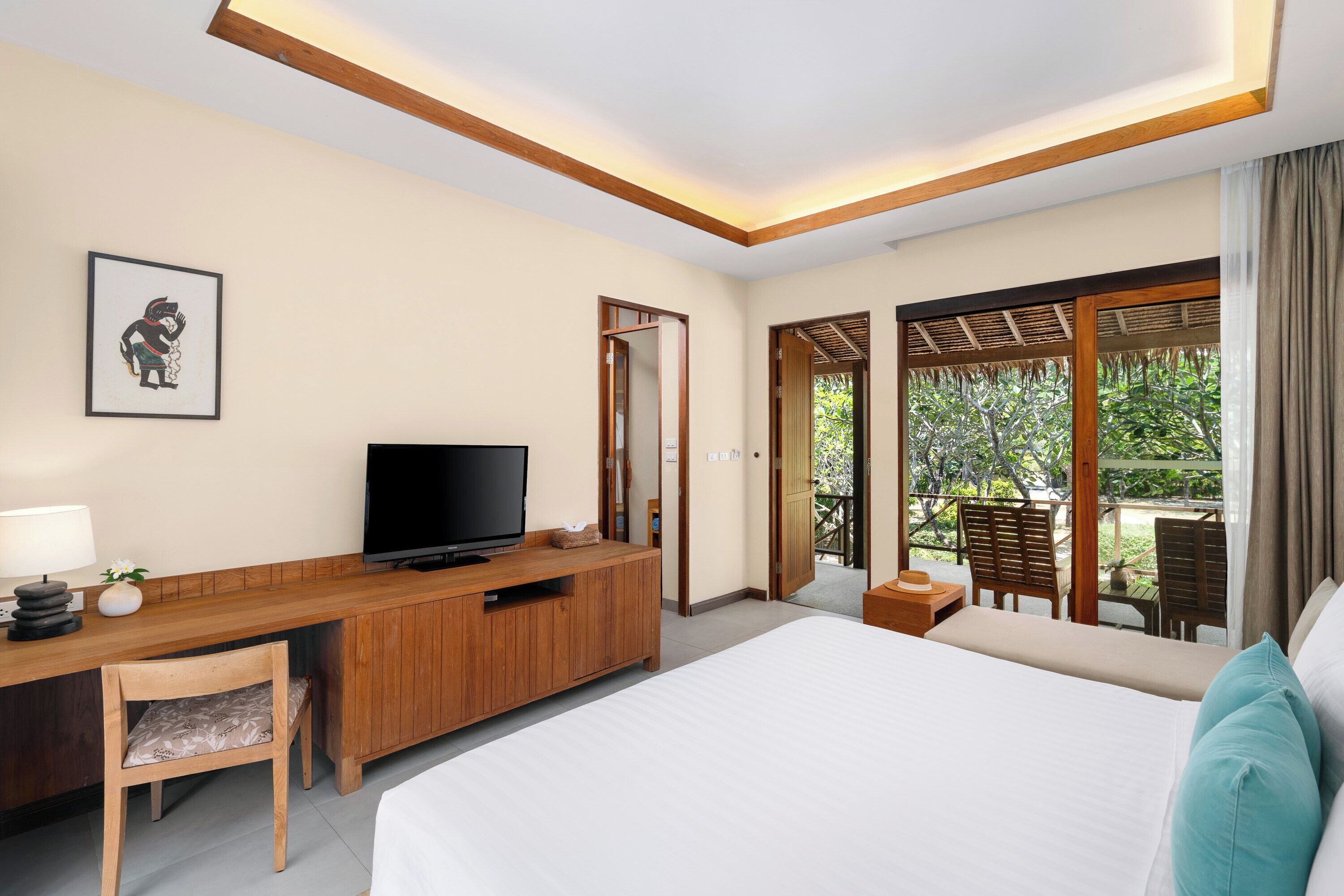 Habitación de hotel con cama, escritorio de madera con televisor, una silla y vista al exterior a través de amplias ventanas.