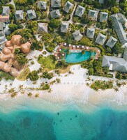 An aerial view of a resort with overwater bungalows, a central pool, and a beach.