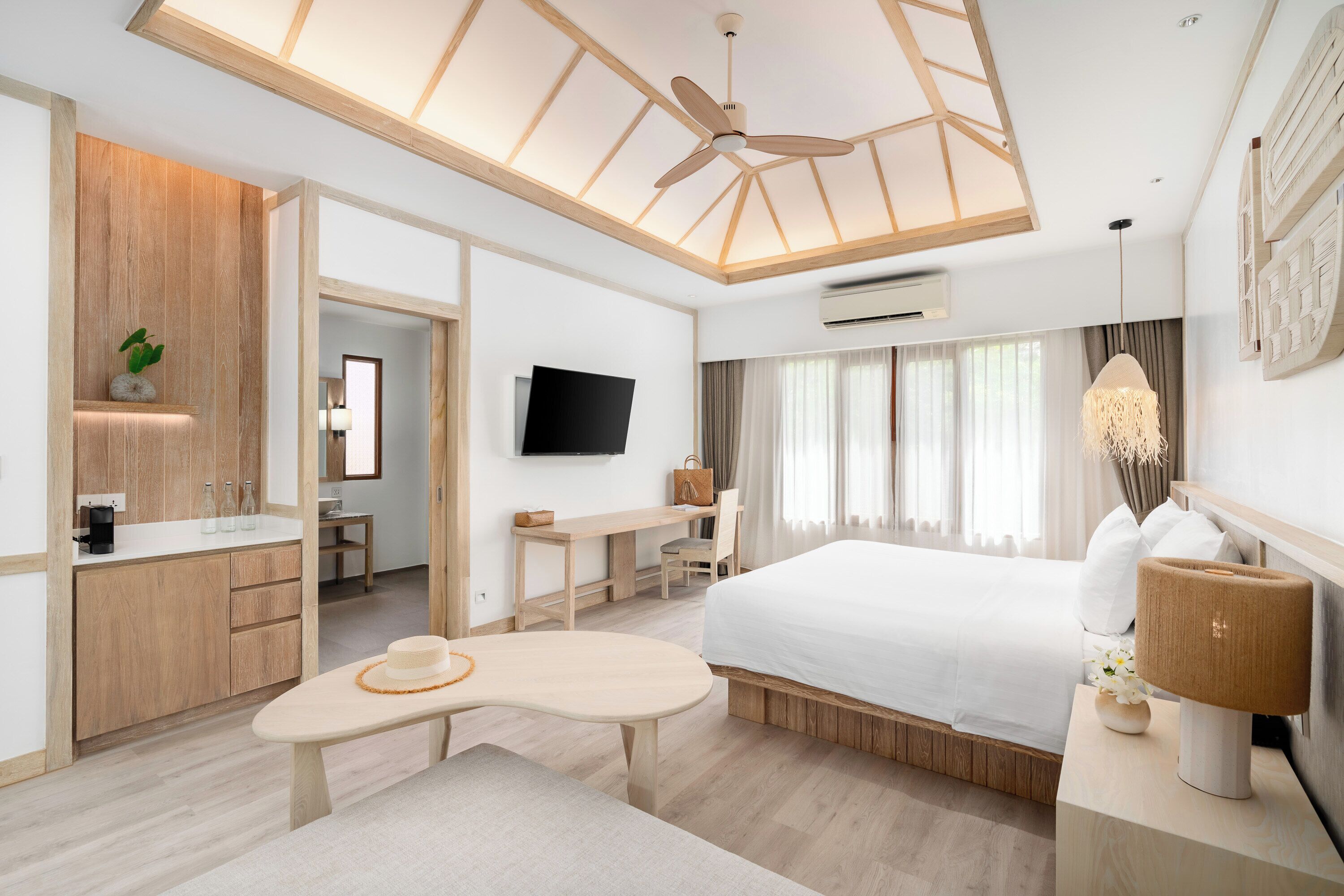A modern hotel room with a wooden ceiling, a bed, a desk, a TV, and a bathroom with wooden cabinets.