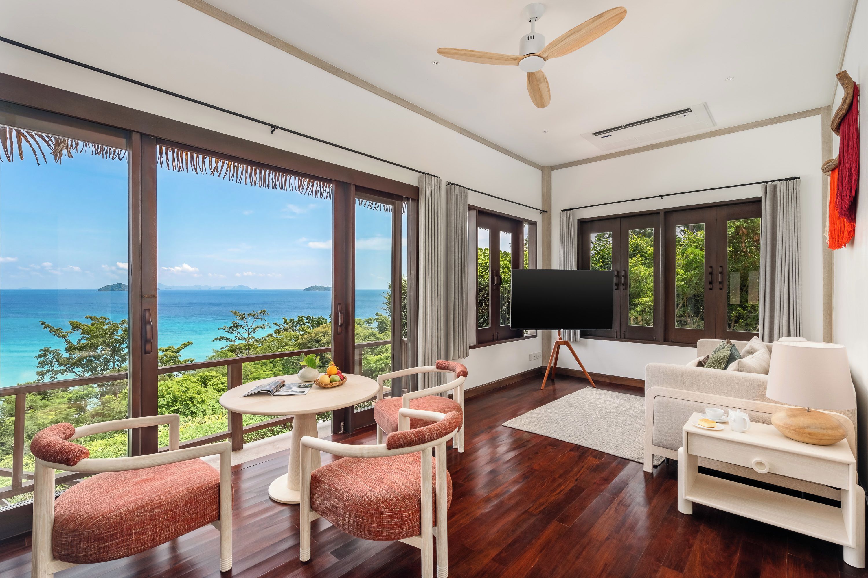 Una sala de estar moderna con un televisor grande, piso de madera y vista al océano.