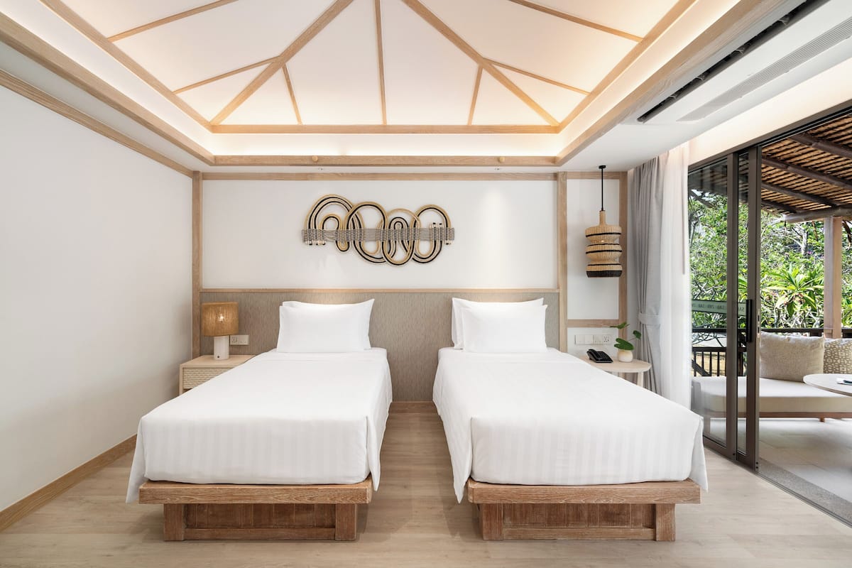 Une chambre d’hôtel moderne avec deux lits, une lucarne, une œuvre d’art accrochée au mur, une petite table avec une lampe, et une vue sur la verdure à l’extérieur.