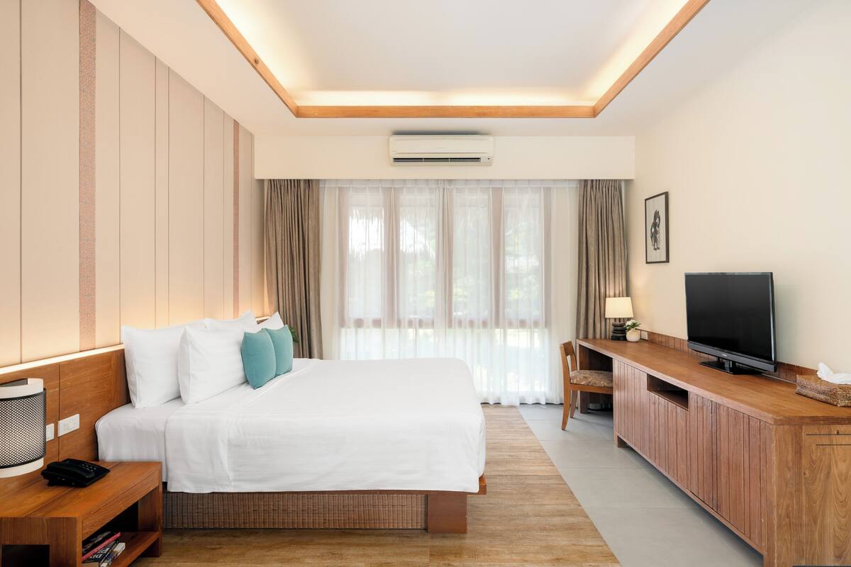 Une chambre d’hôtel avec un lit, une télévision, un bureau et une fenêtre avec des rideaux.
