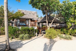 A traditional thatched-roof house with a wooden veranda, surrounded by tropical vegetation and a clear sky. - SAii Phi Phi Island Village (Ko Phi Phi)