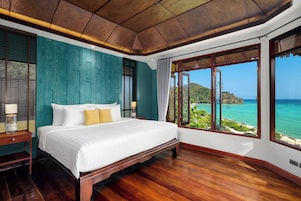 A spacious bedroom with a large bed, wooden flooring, and a view of the ocean.