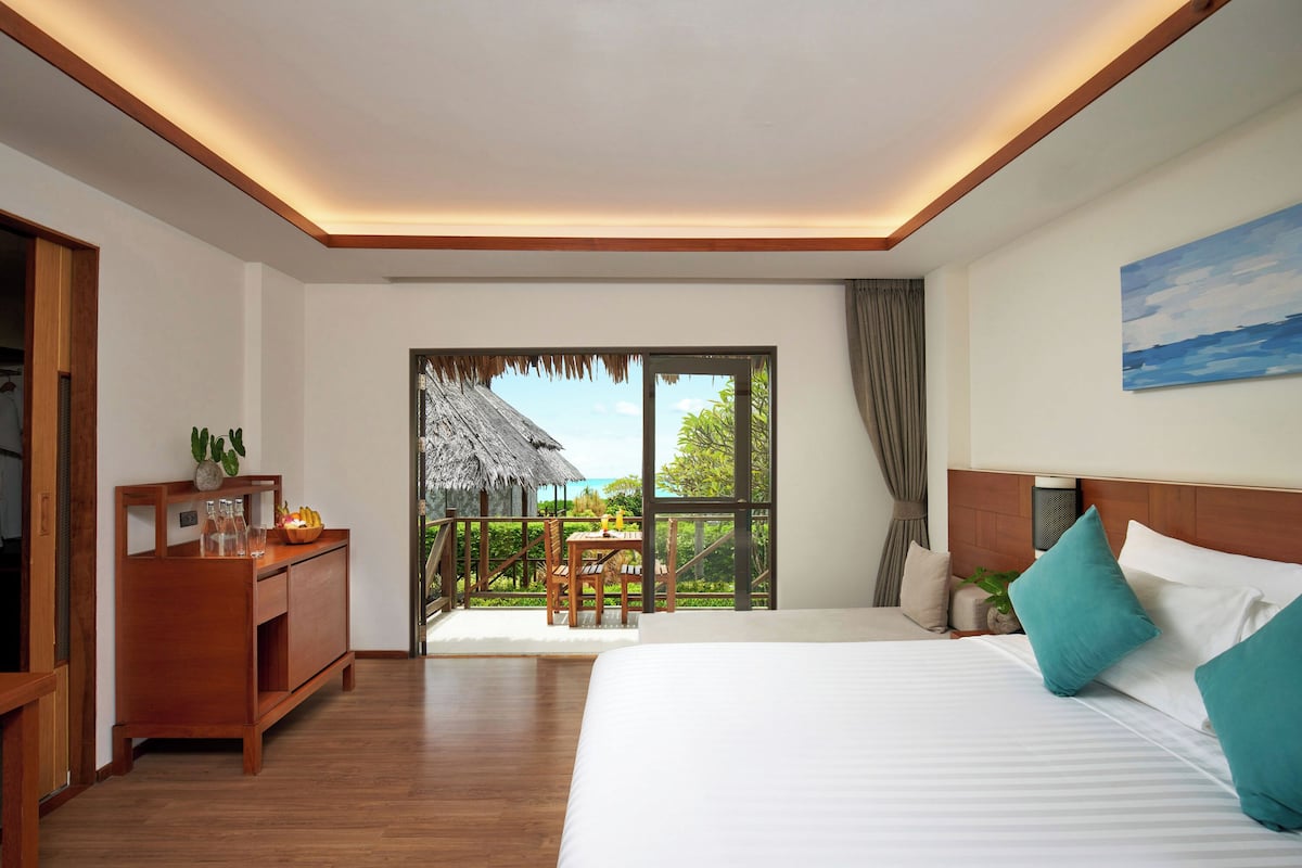 Une chambre d’hôtel avec un grand lit, des meubles en bois, un balcon avec vue et un tableau au mur.