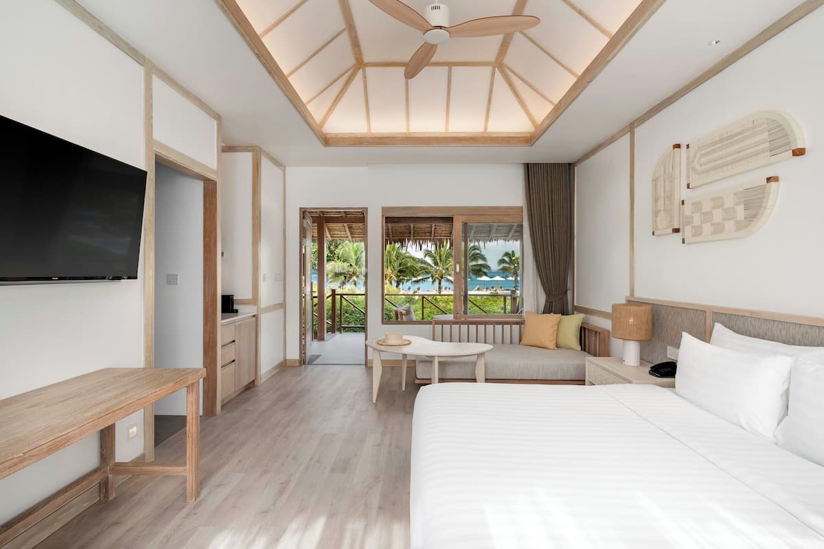 Une chambre d’hôtel avec un grand lit, une télévision, un bureau et un balcon offrant une vue sur les palmiers.