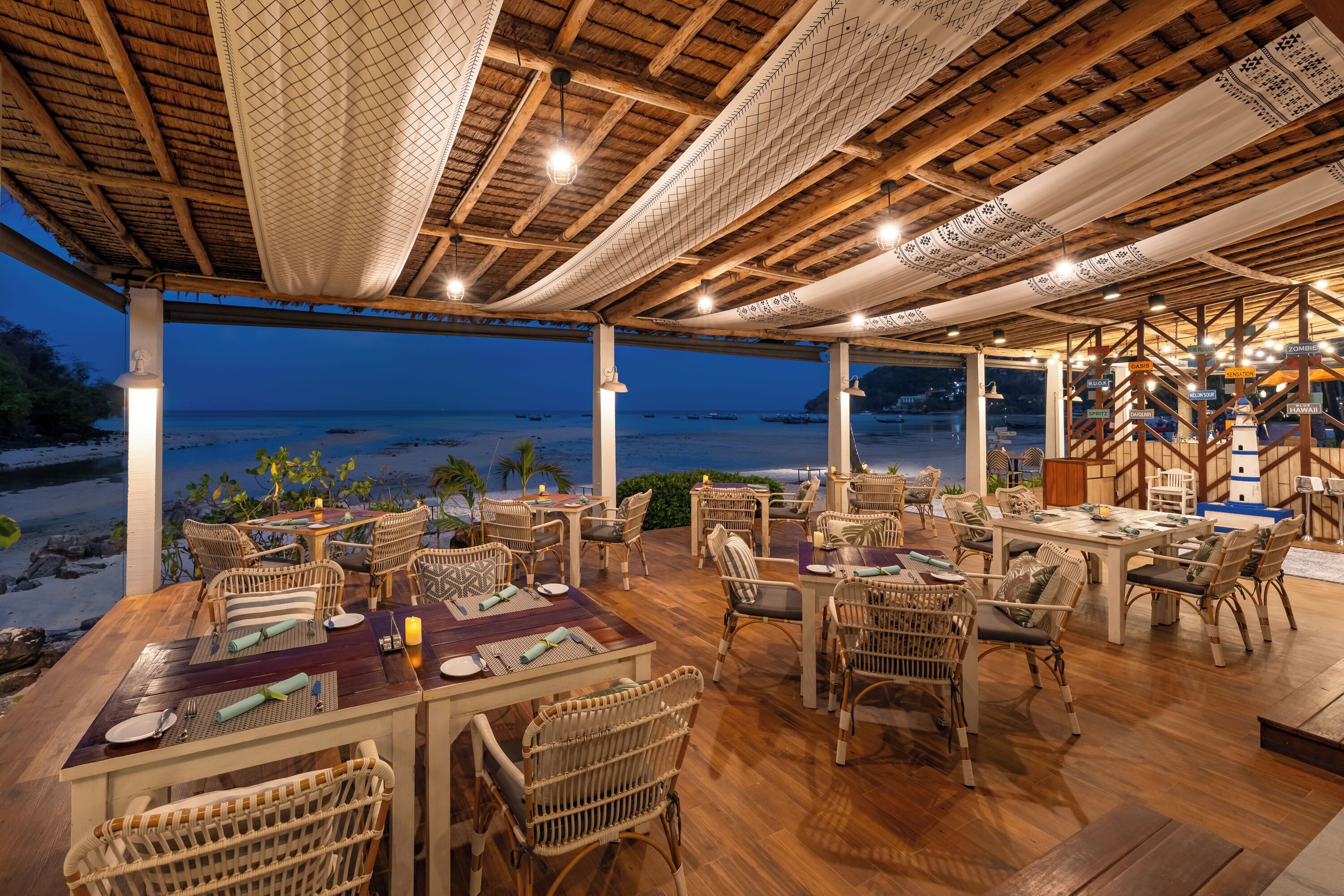 An outdoor dining area with wicker furniture and a view of the beach at dusk.