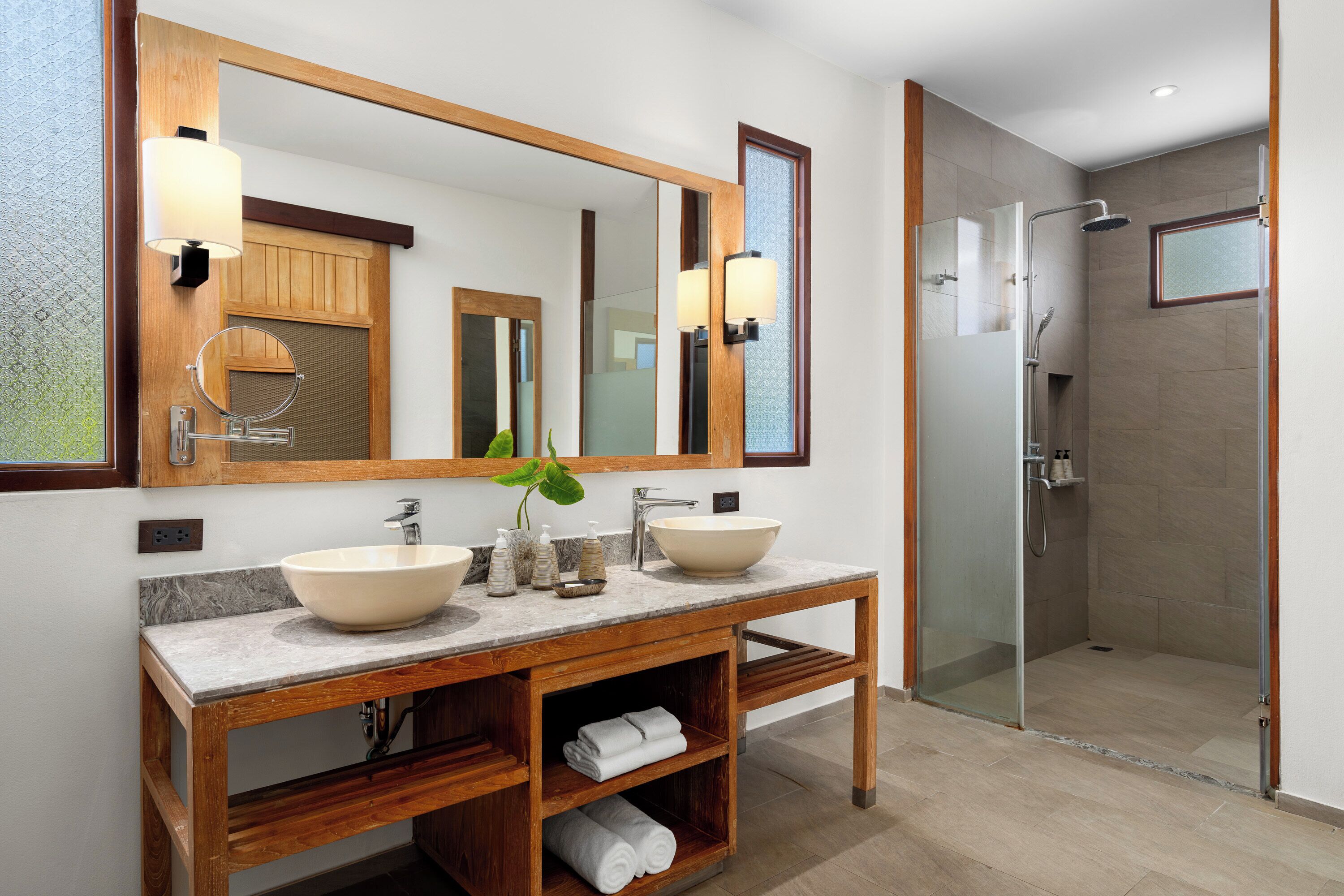 A modern bathroom with two sinks, a large mirror, and a glass-enclosed shower.