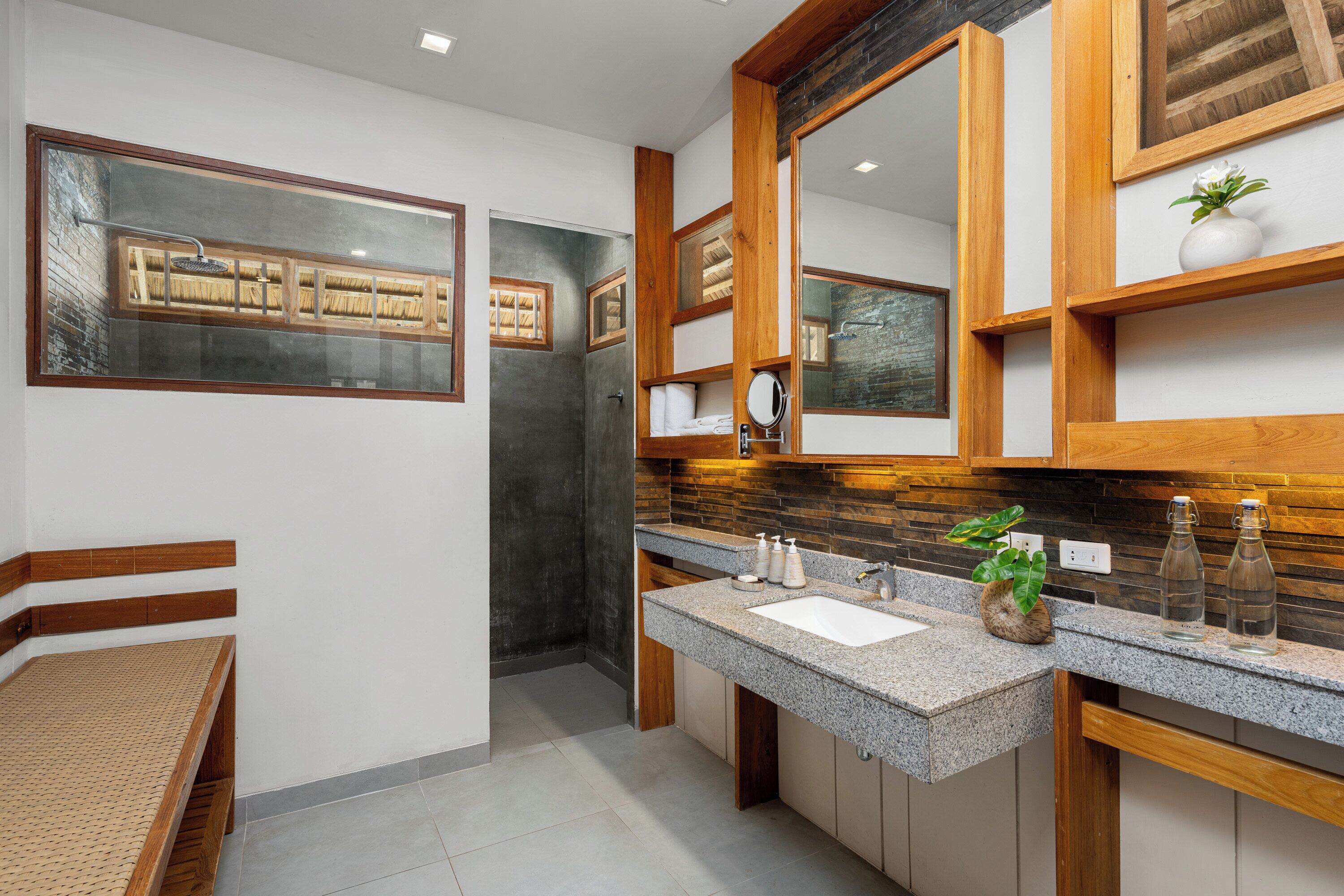 A modern bathroom with a granite countertop, wooden vanity, and a large mirror.