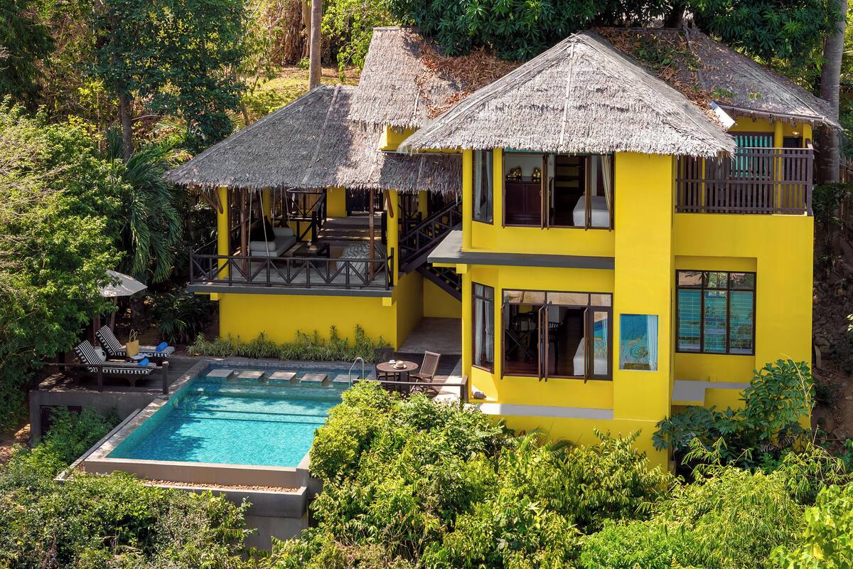 Un bâtiment jaune doté d’une piscine et de structures à toits de chaume.