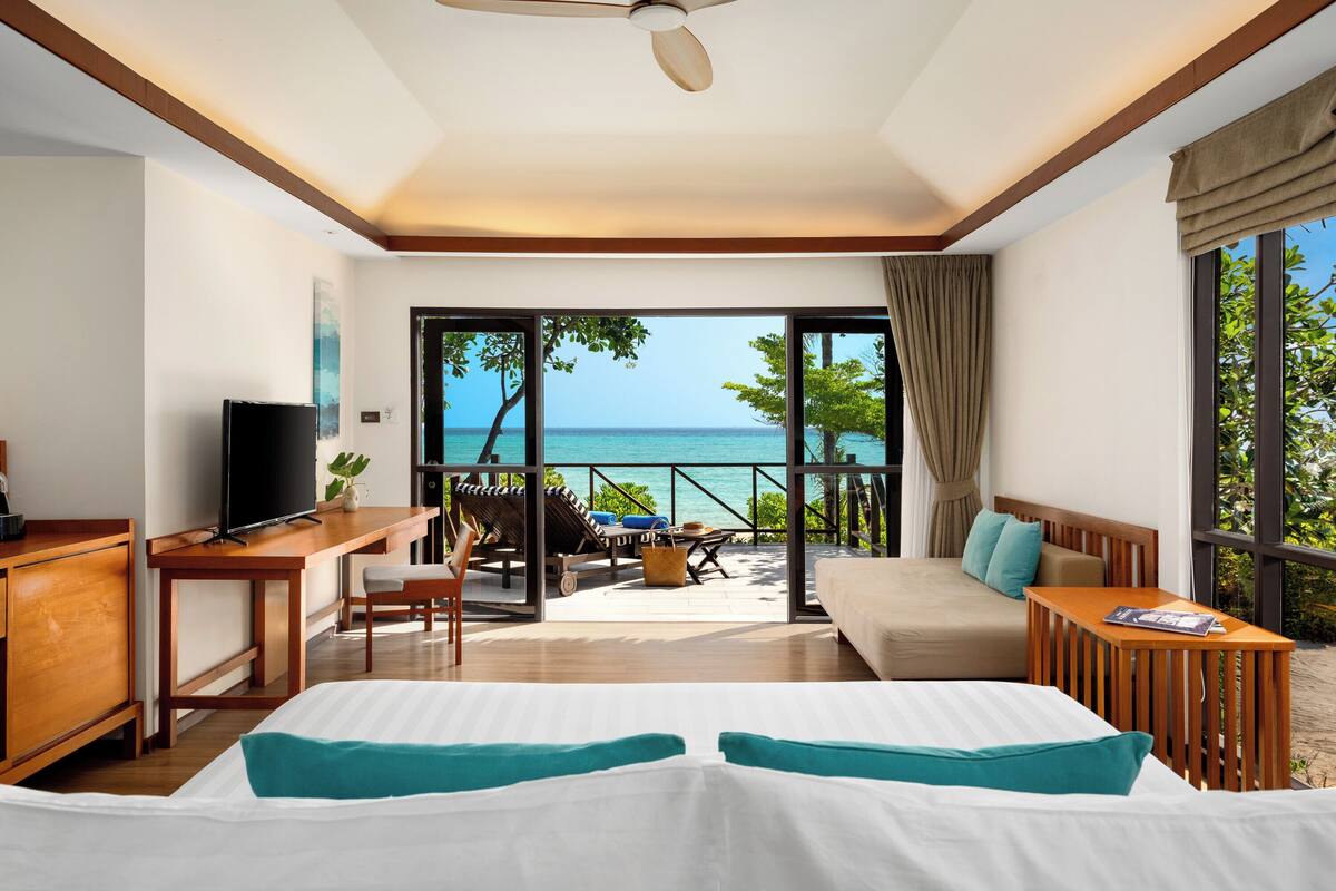 Une chambre d’hôtel comprenant un lit, un bureau, une télévision, un balcon avec vue sur la mer et un canapé.