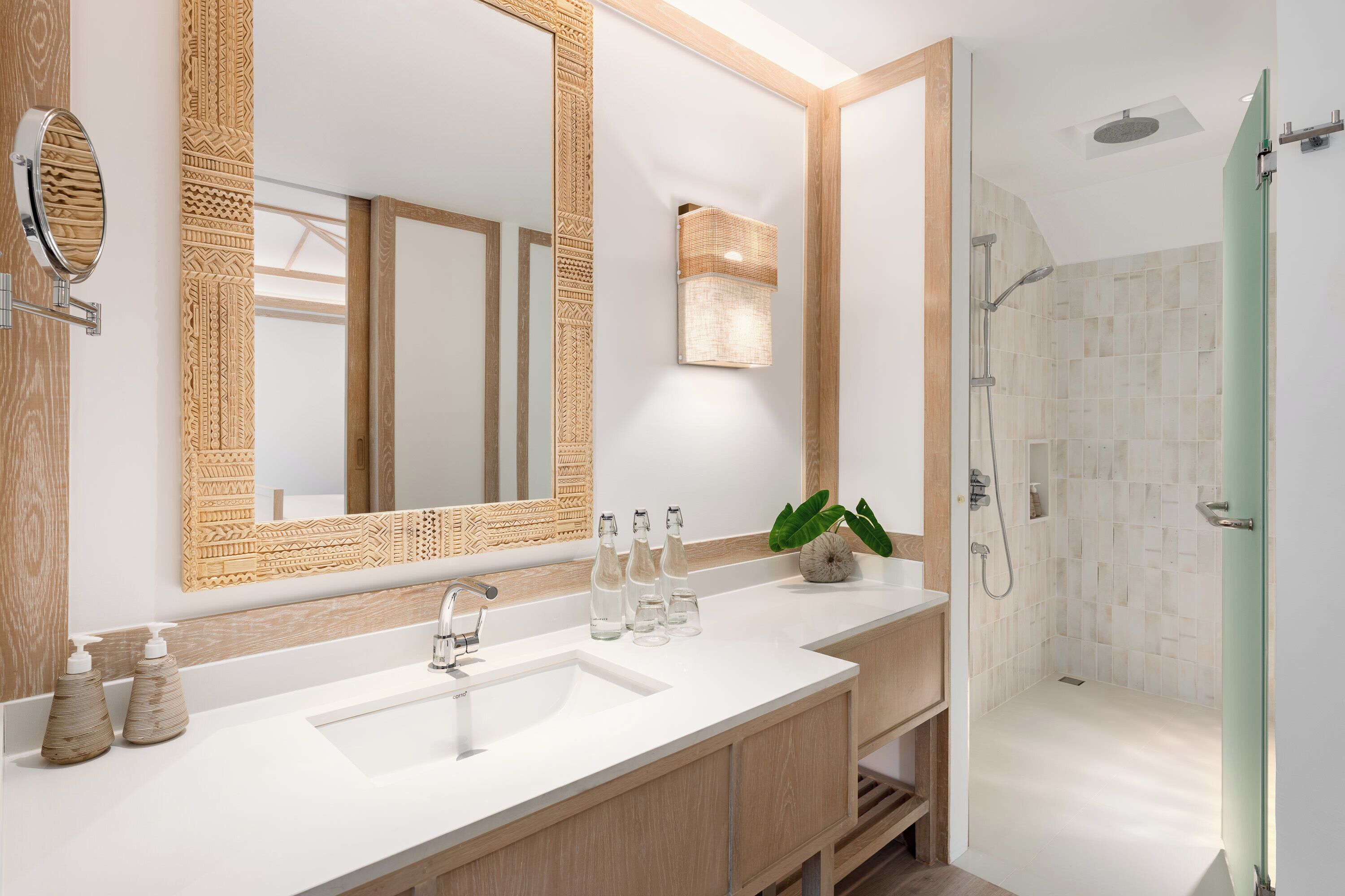 A modern bathroom with a large mirror, a sink, a shower, and a plant.