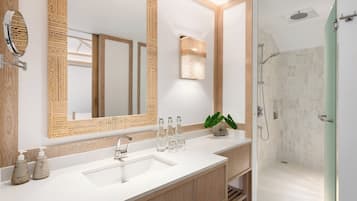 A modern bathroom with a large mirror, a sink, a shower, and a plant.