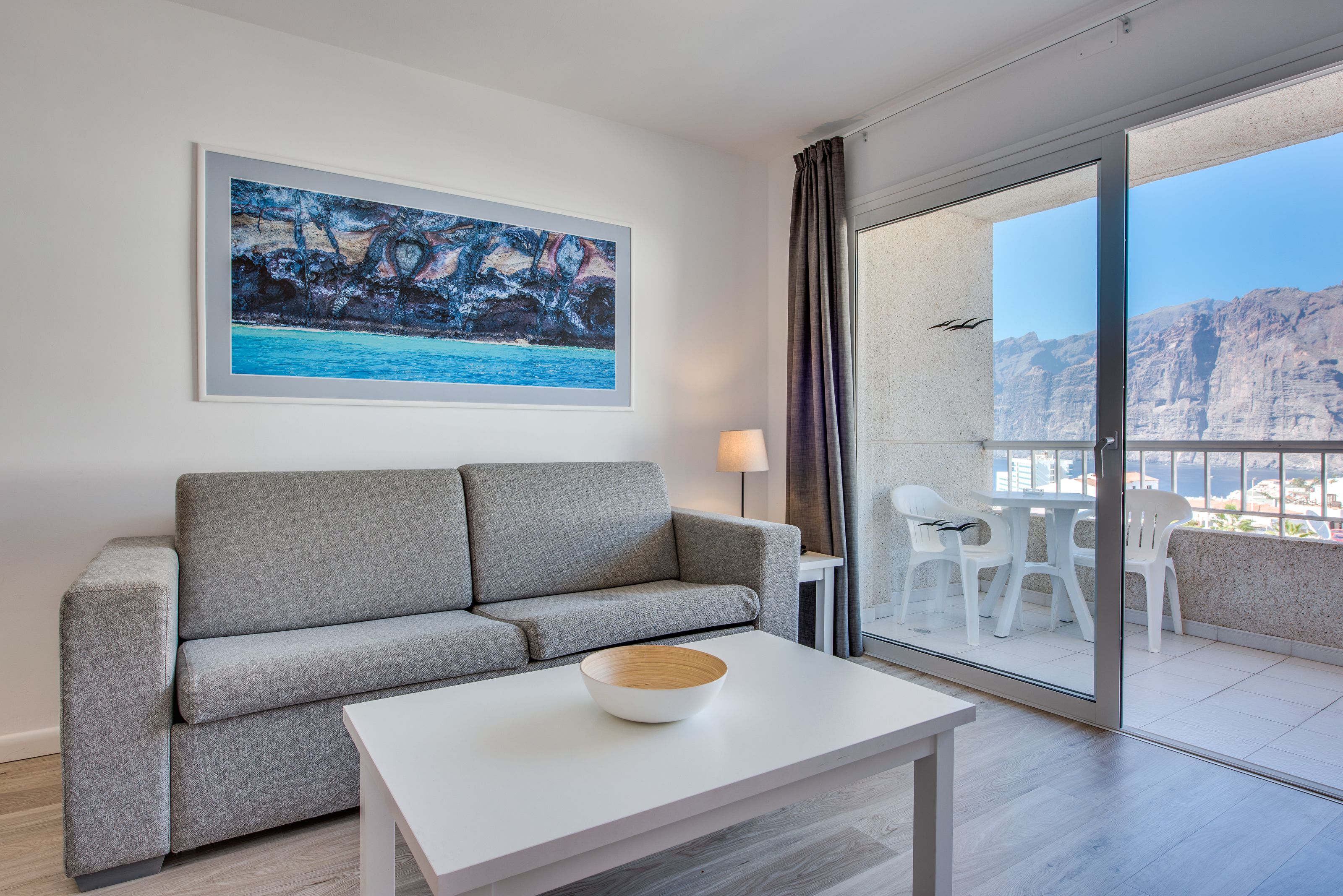 Ein modernes Wohnzimmer mit einem grauen Sofa, einem weißen Couchtisch und einem gerahmten Gemälde einer Küstenlandschaft.