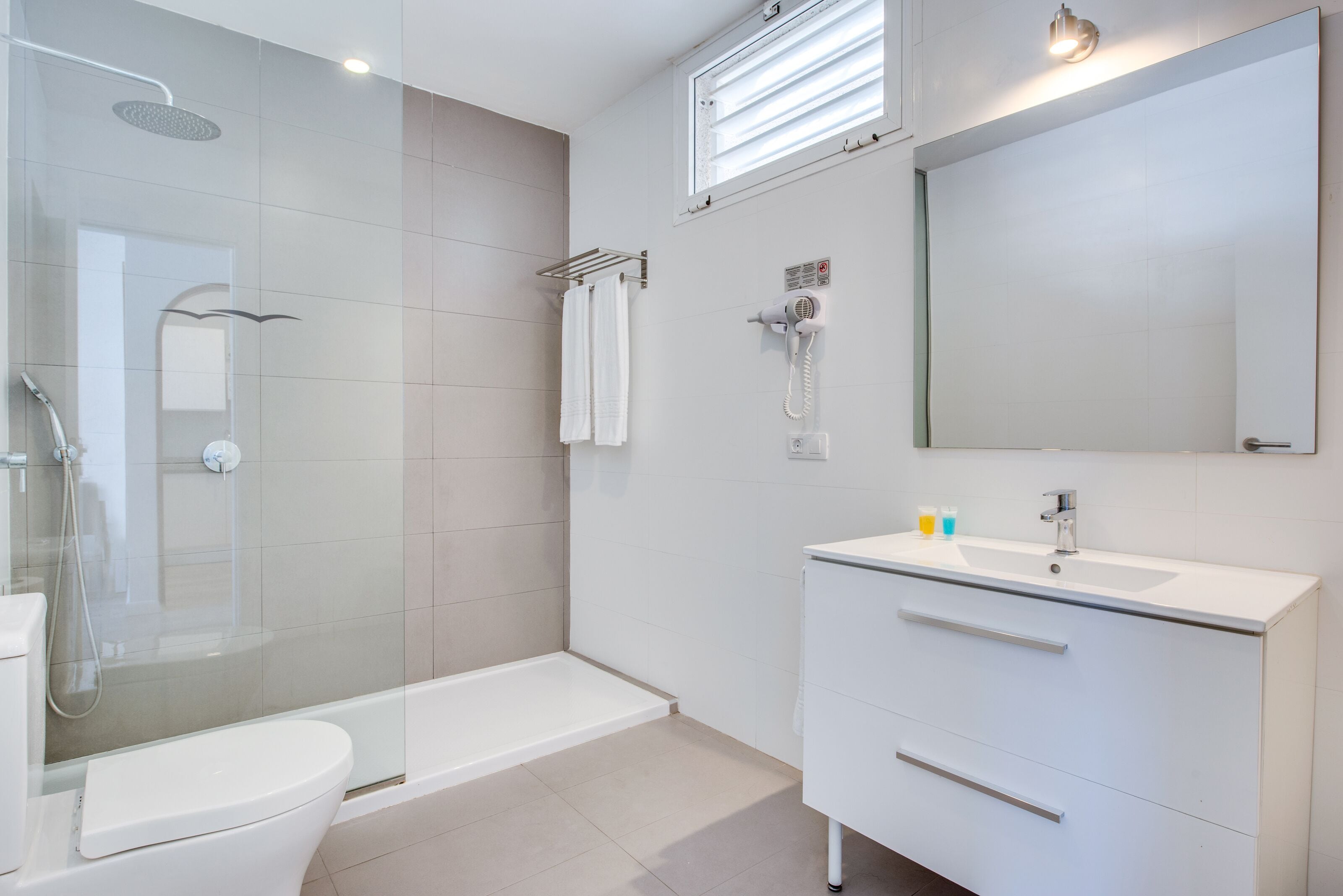 Et moderne badeværelse med et glasvægshus, et hvidt toilet, et badekar og en vask med skuffer.