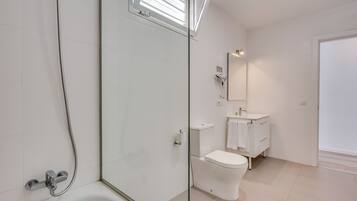 A modern bathroom with a glass shower enclosure, a white toilet, and a vanity with a mirror.