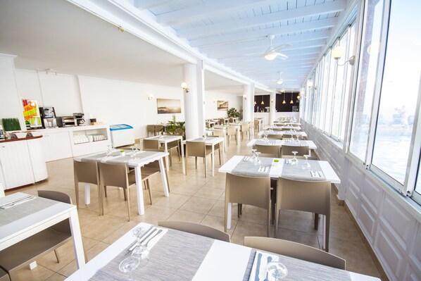Un restaurant spacieux, doté de hauts plafonds et de grandes fenêtres, offrant une vue sur la ville. Les tables sont disposées avec soin et joliment dressées.