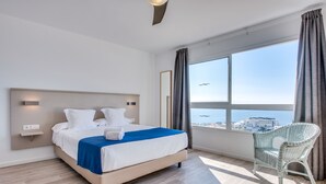 Een moderne hotelkamer met een groot bed, uitzicht op zee en een rieten stoel.