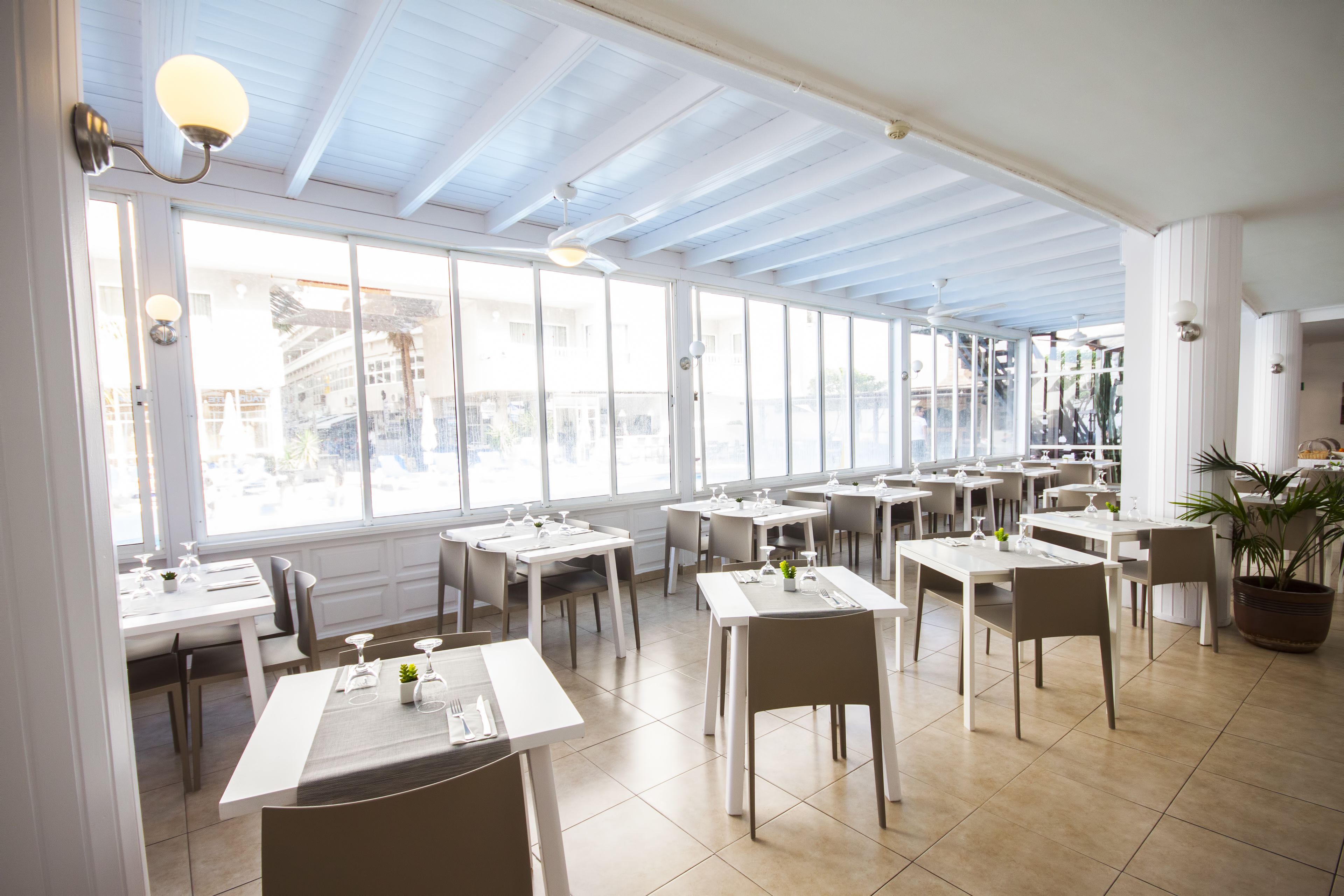Ein geräumiges Restaurant mit großen Fenstern, weißen Tischen und Stühlen.