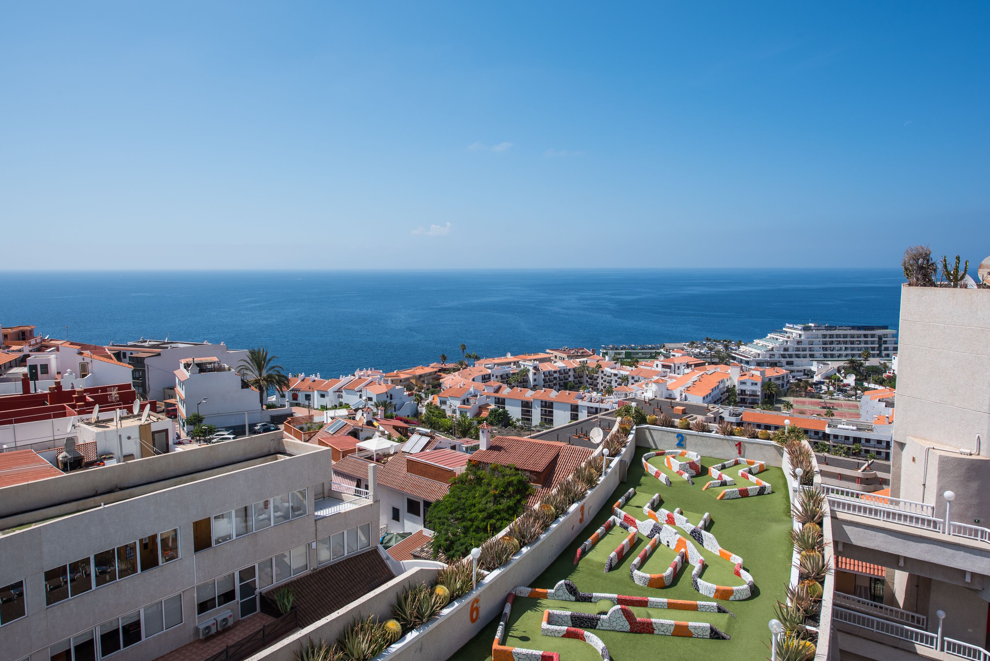 Un hôtel situé sur la côte, doté d’un jardin sur le toit, offrant une vue sur l’océan et présentant une architecture méditerranéenne traditionnelle.