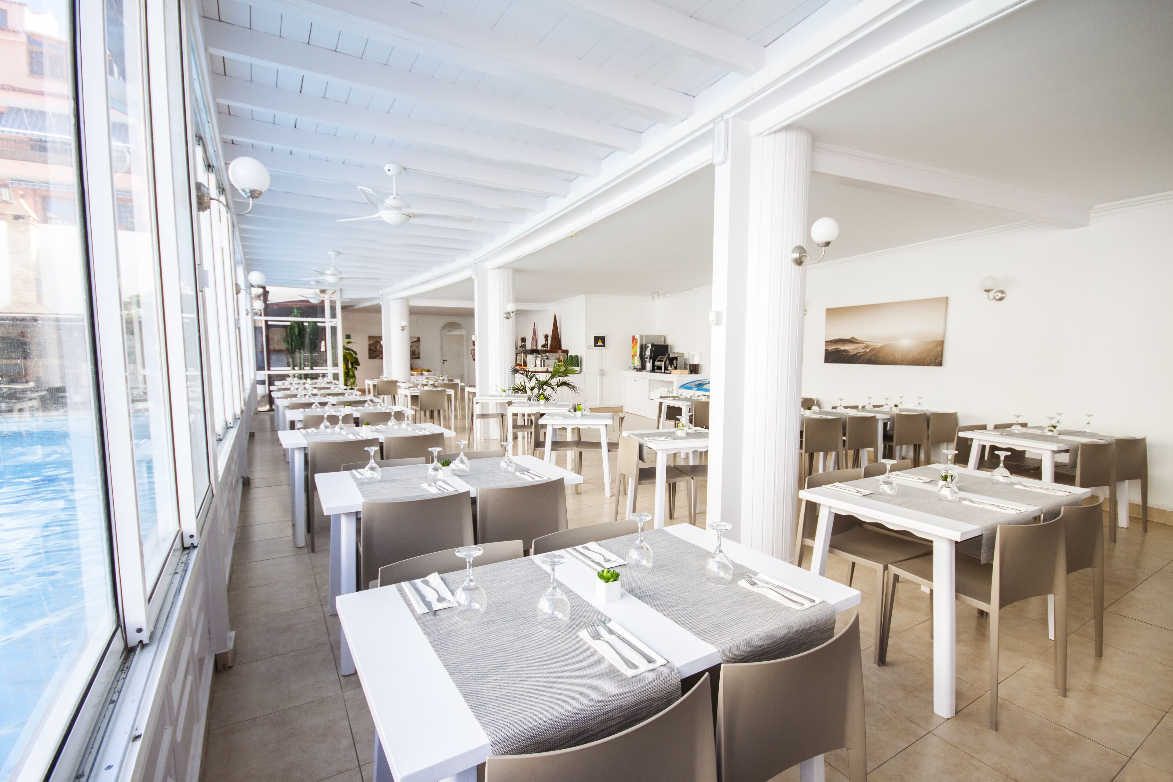 Um restaurante com várias mesas e cadeiras, janelas amplas e vista para a água.