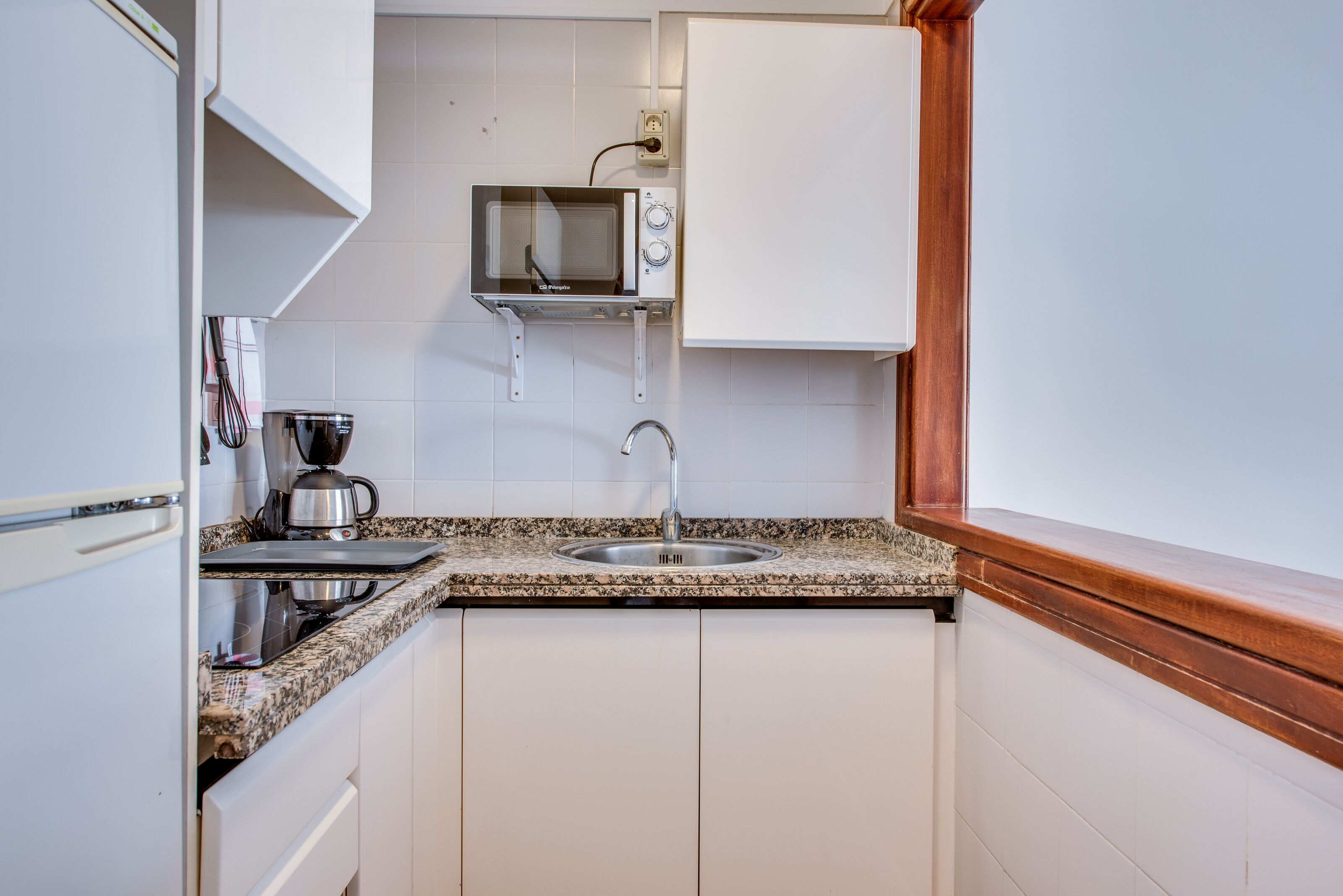 A compact kitchen with white cabinets, a granite countertop, a built-in microwave, and a stainless steel sink.