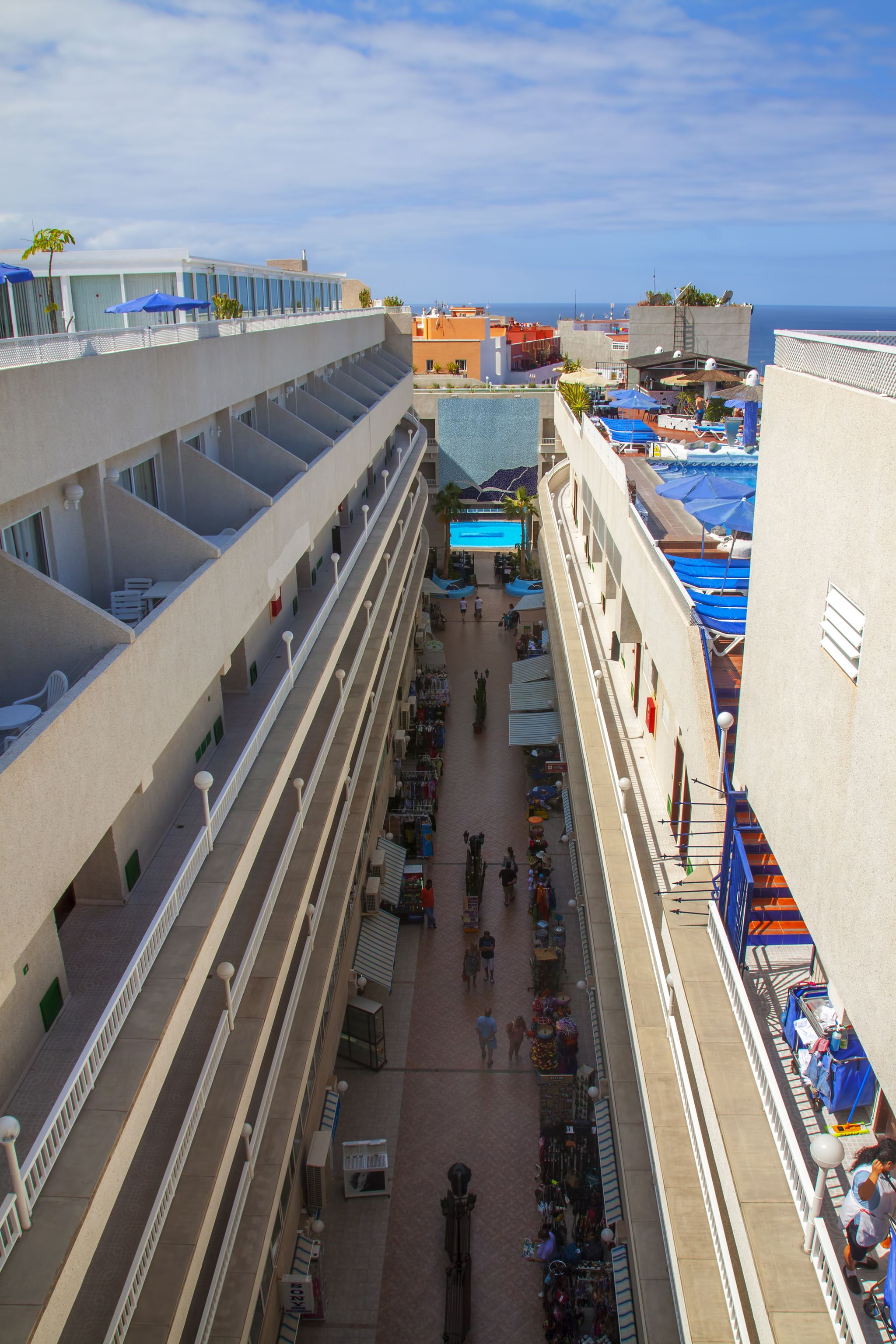 A multi-level hotel atrium with balconies, a pool area, and outdoor seating.