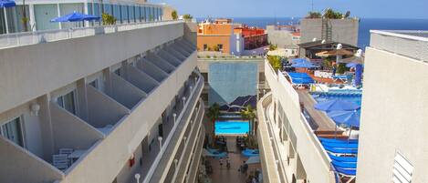 A multi-level hotel atrium with balconies, a pool area, and outdoor seating.