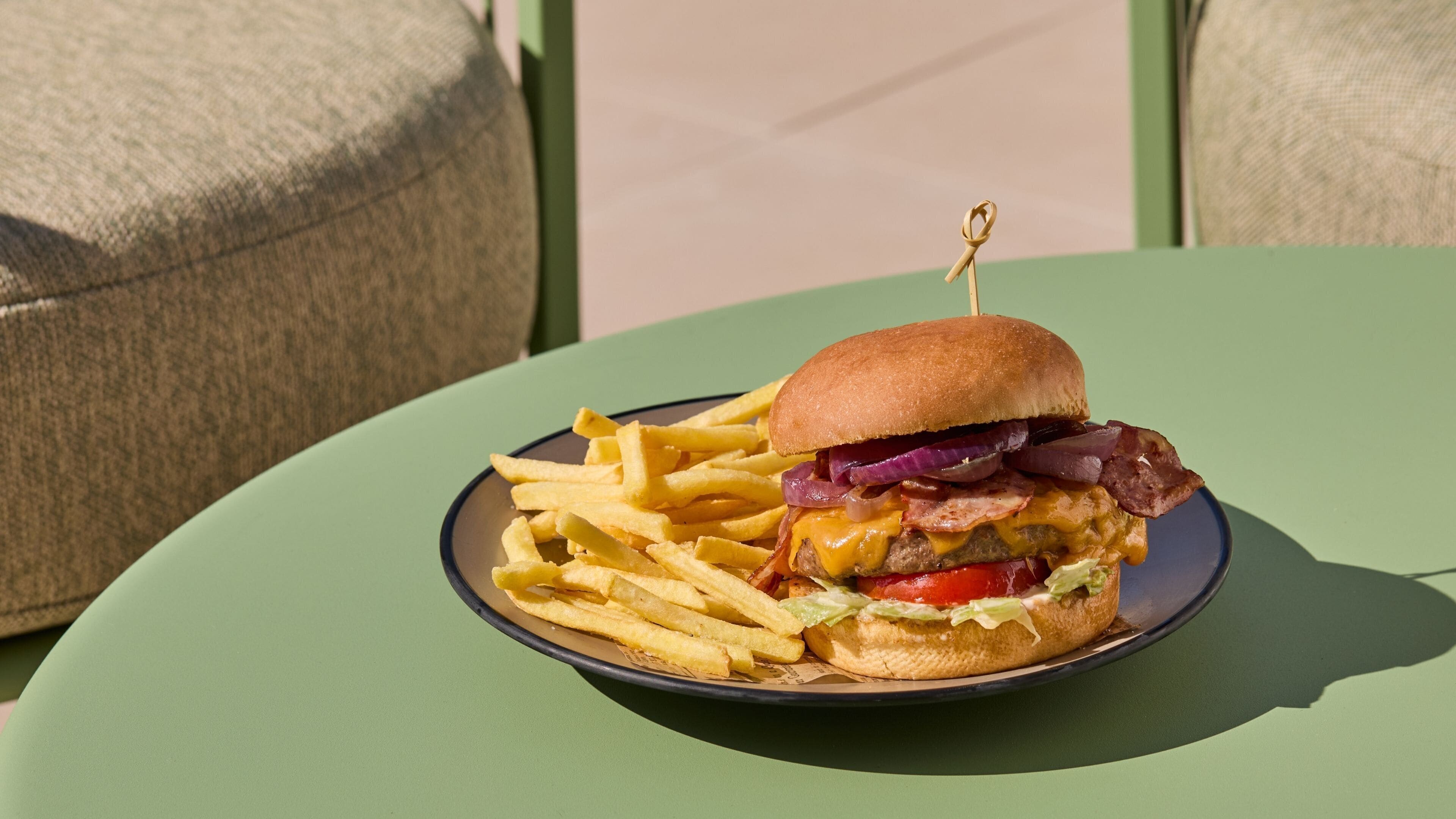 Un plato con una hamburguesa y papas fritas sobre una mesa verde.