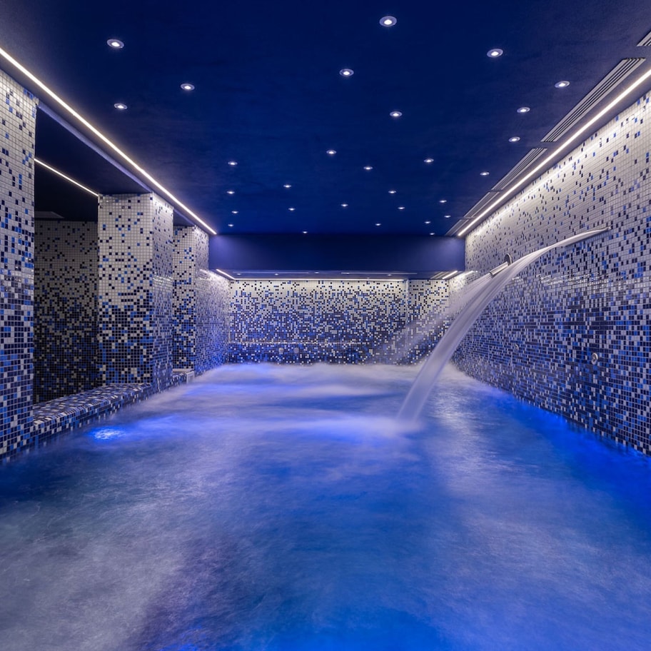 A spa with a blue-tiled floor and walls, a central water feature, and recessed lighting.
