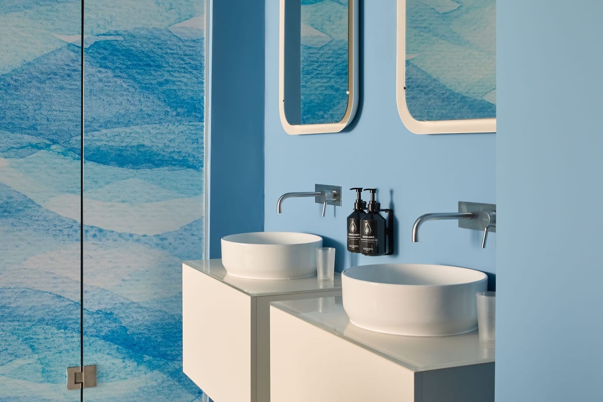 A bathroom with two white sinks, a mirror, and a wall with a blue abstract pattern.