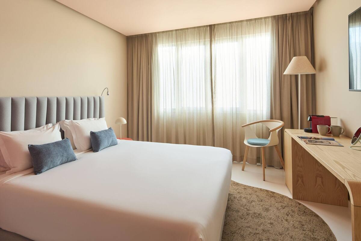 Una habitación de hotel con una cama grande, un escritorio, una silla y una ventana con cortinas.