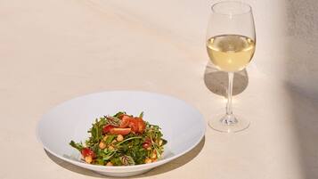 A white plate with a salad and a glass of white wine on a light-colored surface.