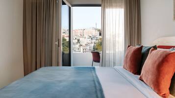 Habitación de hotel con una cama, una silla y vistas a edificios a través del ventanal.