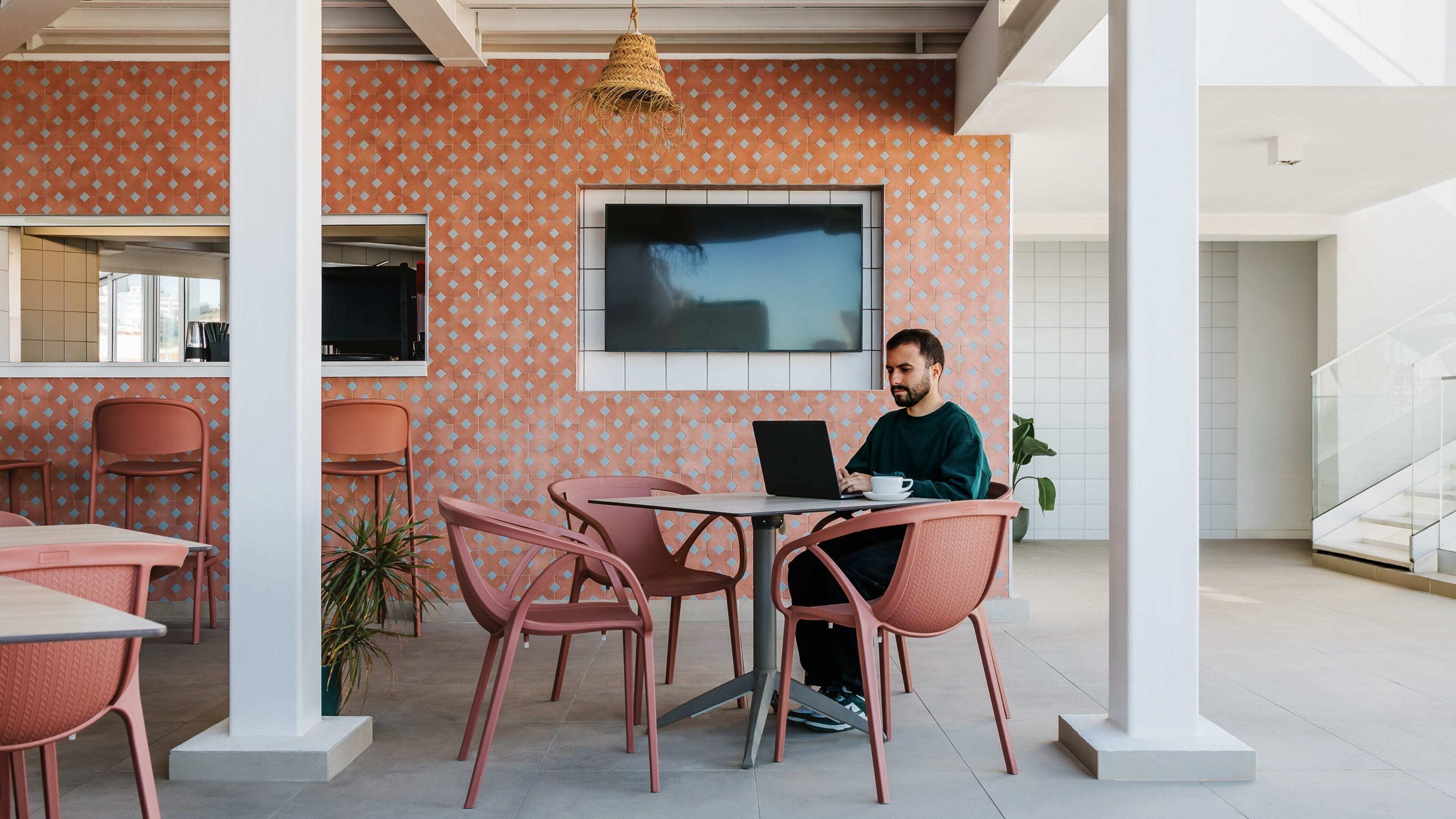Un interior moderno con una pared estampada, un televisor de pantalla plana y una persona trabajando en una mesa con una computadora portátil.