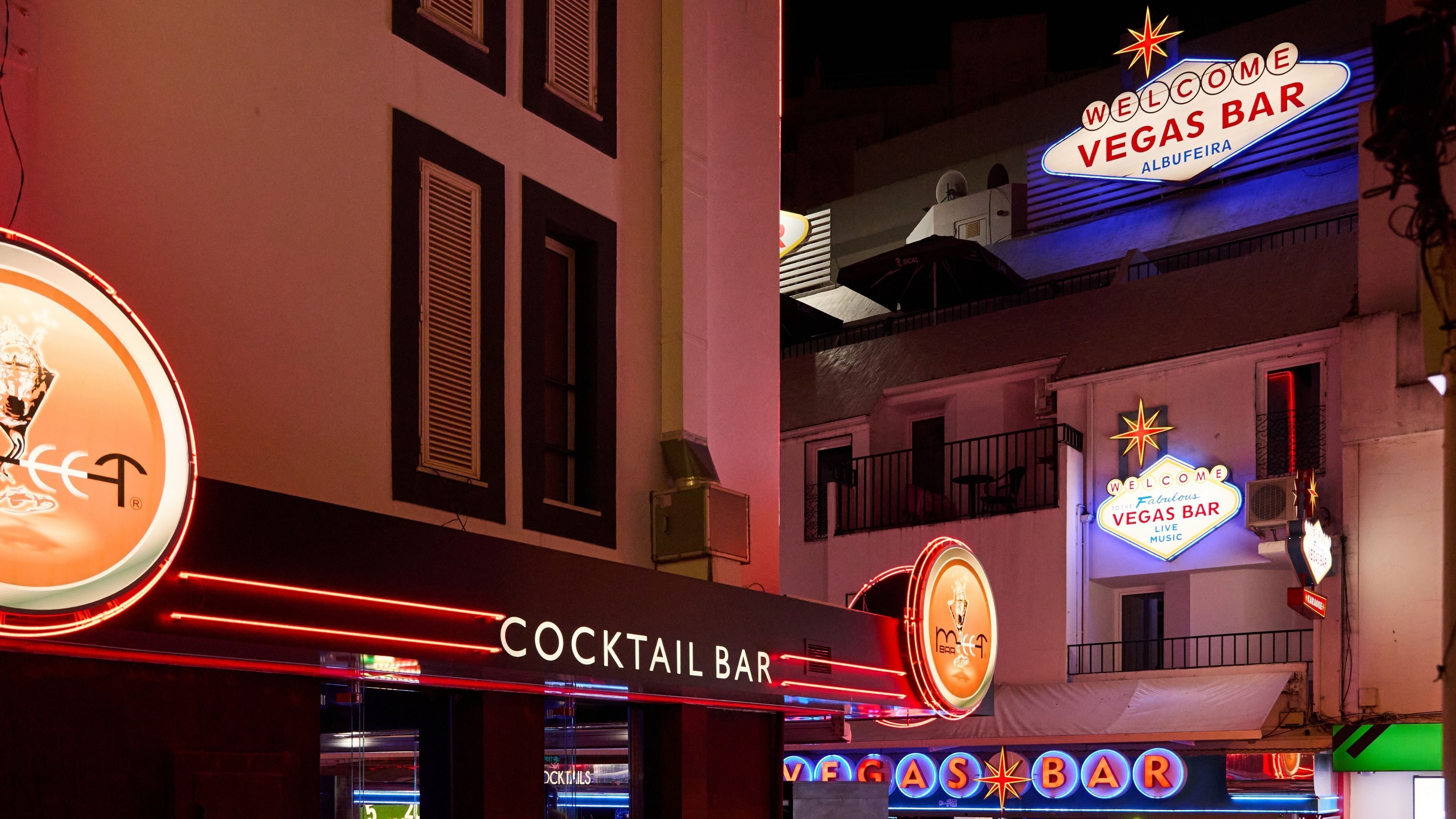 A cocktail bar with neon signs, including "WELCOME VEGAS BAR" and "COCKTAIL BAR".
