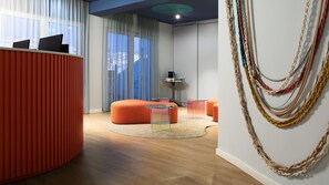 A modern room with a red accent wall, a round orange seating area, a glass coffee table, and a wall-mounted macrame decoration.