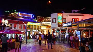 A bustling street scene at night with various shops and restaurants, including an Indian Taj and a steak house.