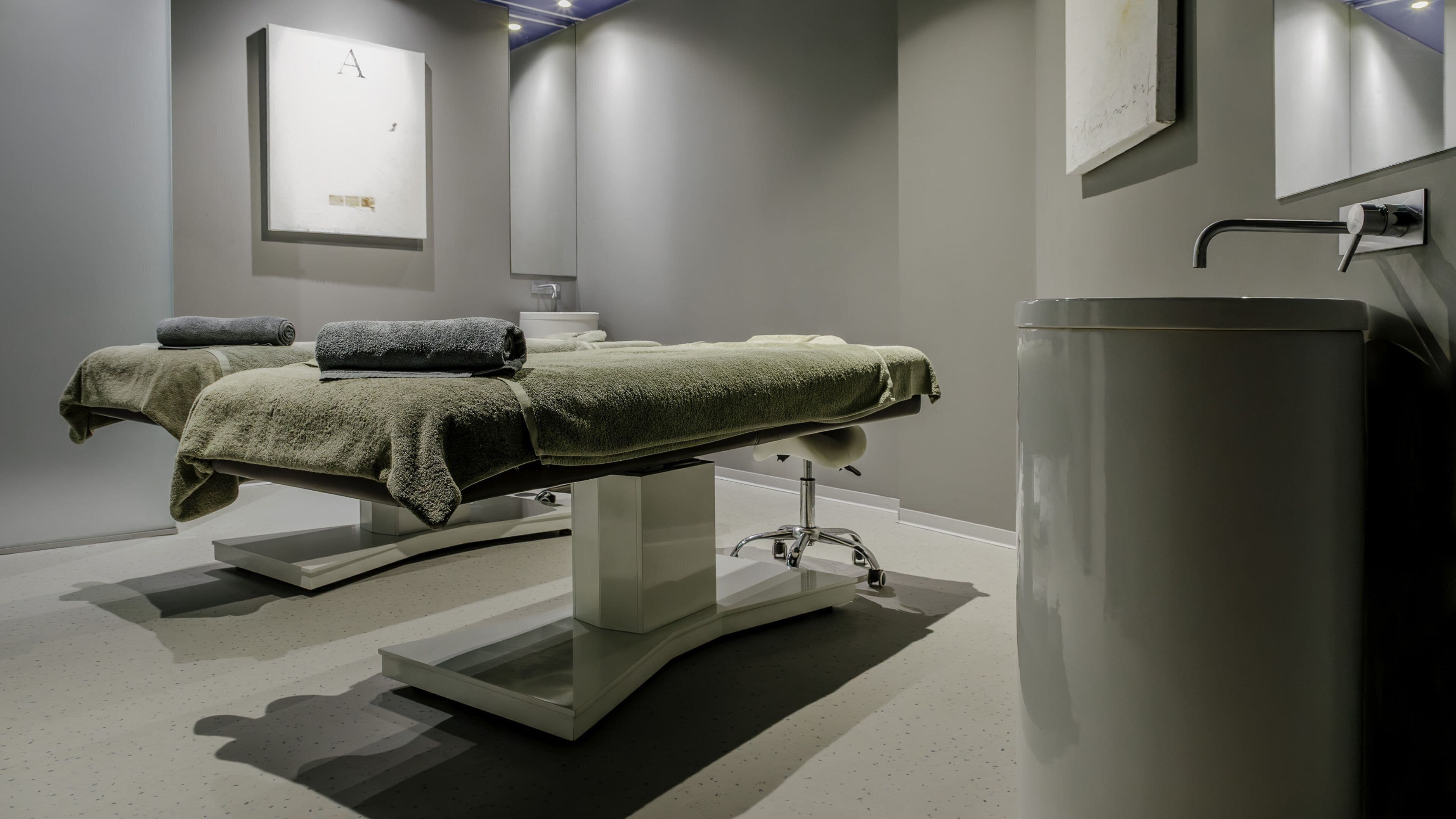 A modern bathroom with a large sink, two towel-wrapped massage tables, and a minimalist design.