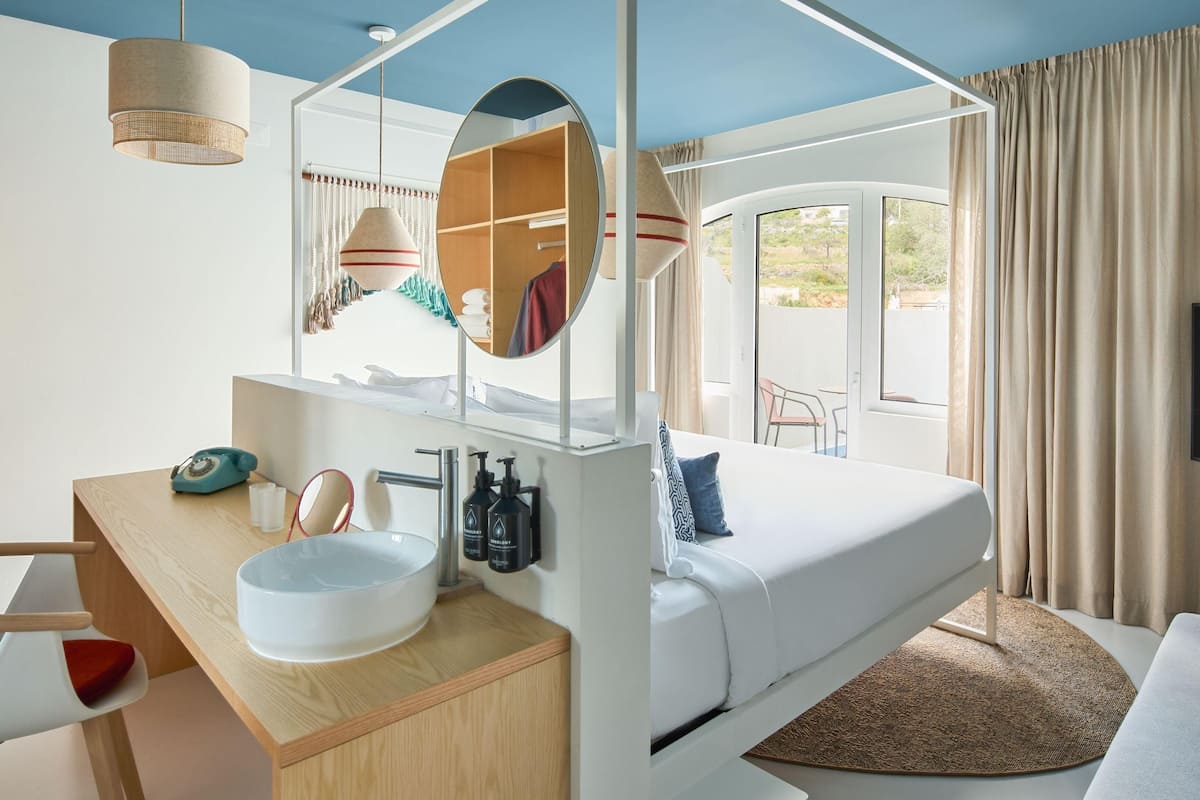A modern hotel room with a bed, a desk with a sink, a mirror, and a TV.